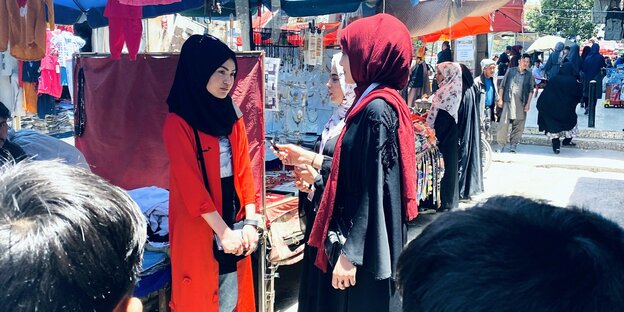 Zwei Junge Frauen interviewen eine andere junge Frau vor einem Marktstand