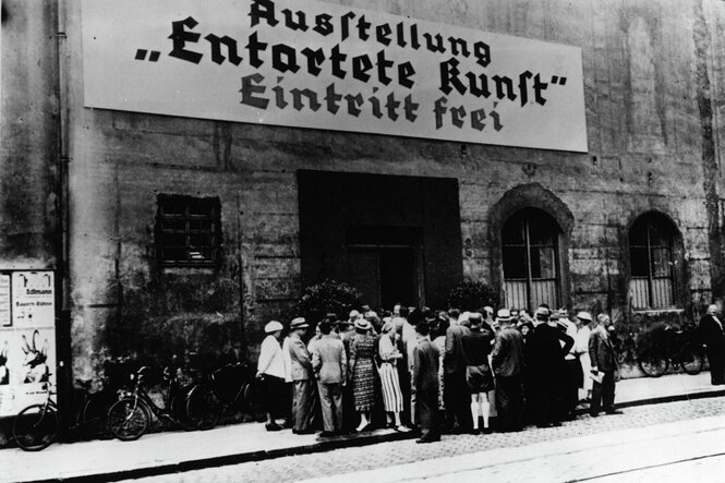 "Ausstellung Entartete Kunst Eintritt frei" steht auf einem großen Plakat über dem Eingangstor, darunter eine Menge in Sommerkleidung