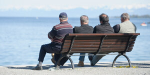 Vier Männer sitzen auf einer Bank an einem See
