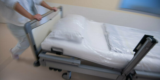 Eine Krankenpflegerin schiebt ein Krankenbett durch einen Gang