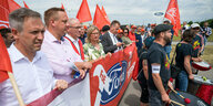 Blick von schräg auf eine Gruppe von Trommlern und eine Reihe Männer und Frauen hinter einem Banner mit Ford-Logo