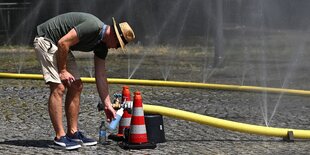 Ein mann füllt eine Wasserflasche mit Wasser an einem Schlauch an der Straße