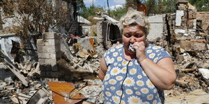 Eine Frau mit Margeriten-Bluse weint vor einem zerstörten Wohnhaus