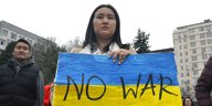 Eine frau hält ein blau-gelbes Plakat mit der Aufschrift "NO WAR"