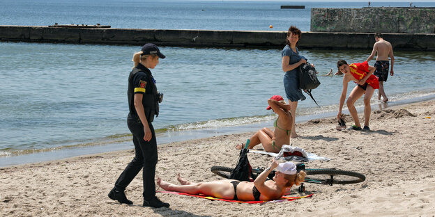 Eine Polizistin warnt Frauen, die sich am Strand von Odessa sonnen