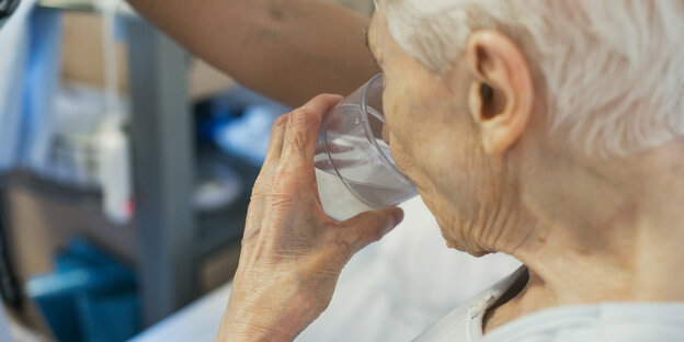 An elderly woman drinks water from a glass.