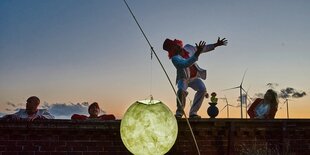 Vier Schauspieler befinden sich auf einer Mauer. Vor ihnen befindet sich im Abendlicht ein Lampion, das den Mond darstellen soll.