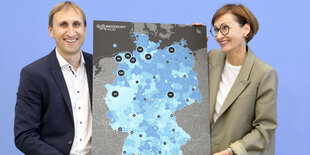 Ein Mann und eine Frau halten ein Plakat zum Wasserstoffatlas hoch