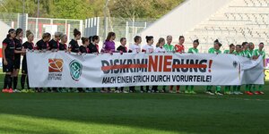 Fußballerinnen stellen sich in einer Reihe auf und zeigen ein Transparent gegen Diskriminierung