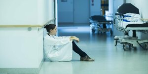 Eine erschöpfte, junge Ärztin sitzt im Krankenhaus-Flur auf dem Boden.