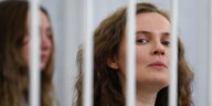 Eine junge Frau reckt ihren Kopf hinter Gitterstäben