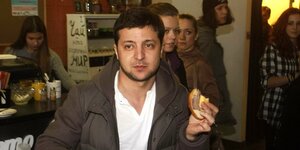 Wolodimir Selenski steht in einem Café mit einem Brötchen in der Hand