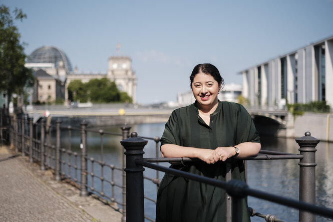 Eine Frau steht auf einer Brücke. Im Hintergrund der Reichstag