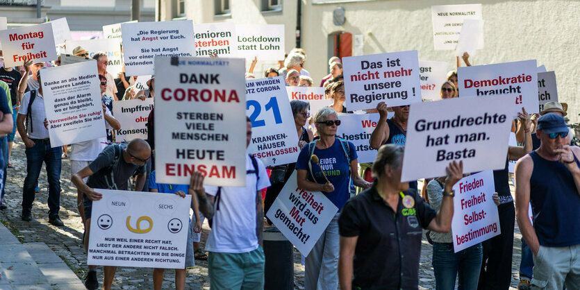 Mehrere Menschen protestieren und halten beschriftete Plakate in die Luft.