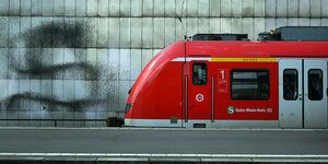 Ein roter Regionalzug steht an einem Bahnsteig. Hinter ihm ist eine Wand zu sehen, auf die ein großes schwarzes S gesprayt ist
