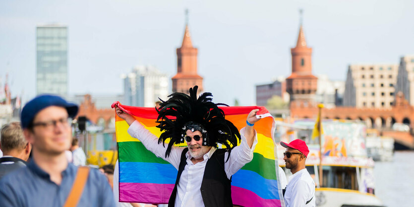 Ein Mann steht mit Regenbogenfahne vor der Oberbaumbrücke