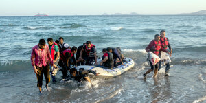 Menschen mit Schwimmwesten springen von einem Schlauchboot auf den Strand