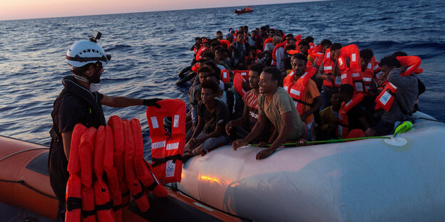 Ein Seenotretter verteilt Rettungswesten an Migranten im Boot