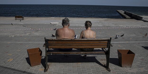 Zwei Menschen sitzen auf einer Bank am Meer