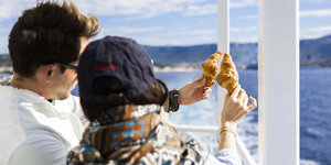 Zwei Touristen halten zwei Croissants in den Händen