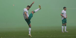 Ein Spieler hält sich wärm, schlägt das Bein in die Luft. Ein anderer steht herum