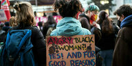 Eine Frau trägt ein Protestplakat auf dem Rücken "Angry black woman? Yes and for good reasons"
