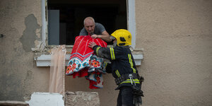 Ein Mann reicht einem Feuerwehrmann eine Decke aus einem Fenster