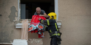 Ein Mann reicht einem Feuerwehrmann eine Decke aus einem Fenster