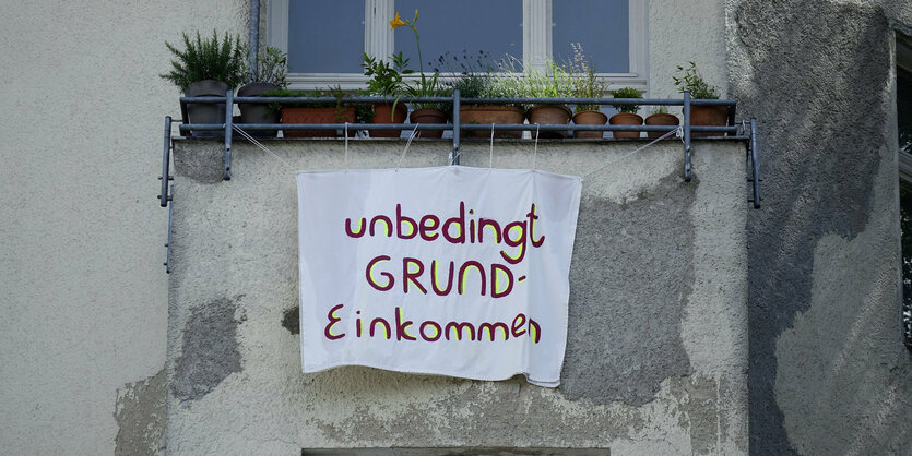 An einem Balkon hängt ein Plakat fürs Grundeinkommen