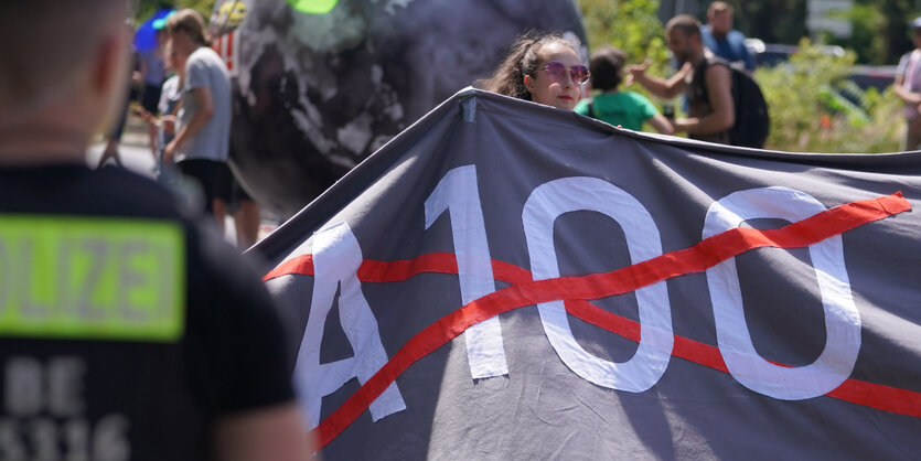 Frau hält Transparent mit durchgestrichenem "A100"