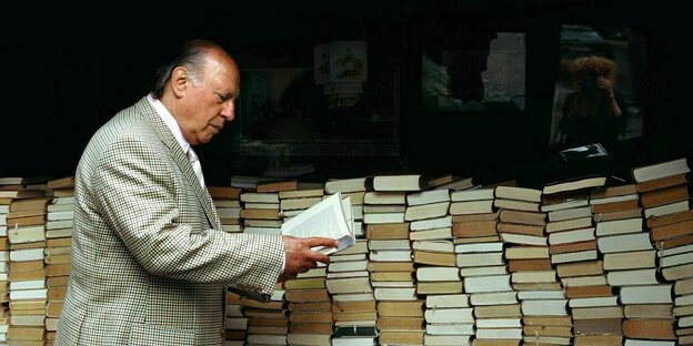 Imre Kertze steht an einem Bücherwagen und schaut interessiert in ein Buch