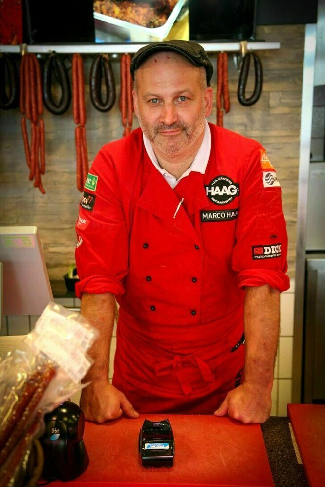 Portrait von Marco Haag in seiner Fleischerei in roter Arbeitskleidung