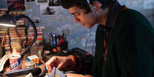 Ein junger Mann sitzt am Schreibtisch, hat Kopfhörer auf und repariert eine Walkman
