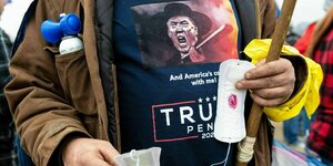 Trumpanhänger trägt ein T-Shirt mit einem wütenden Trump und hält blutige Gesichtsmasken in der Hand
