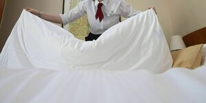 Eine Hotelfachangestellte schüttelt das Bett aus