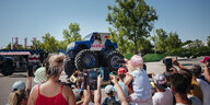 Ein Mann fährt mit einem Monstertruck mit Red Bull-Aufdruck über zwei Autos. Kinder und Erwachsene filmen ihn dabei mit ihren Smartphones