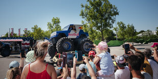 Ein Mann fährt mit einem Monstertruck mit Red Bull-Aufdruck über zwei Autos. Kinder und Erwachsene filmen ihn dabei mit ihren Smartphones