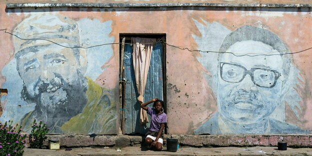 Eine Frau sitzt vor einem alten Propaganda-Wandgemälde mit Fidel Castro und José Eduardo dos Santos