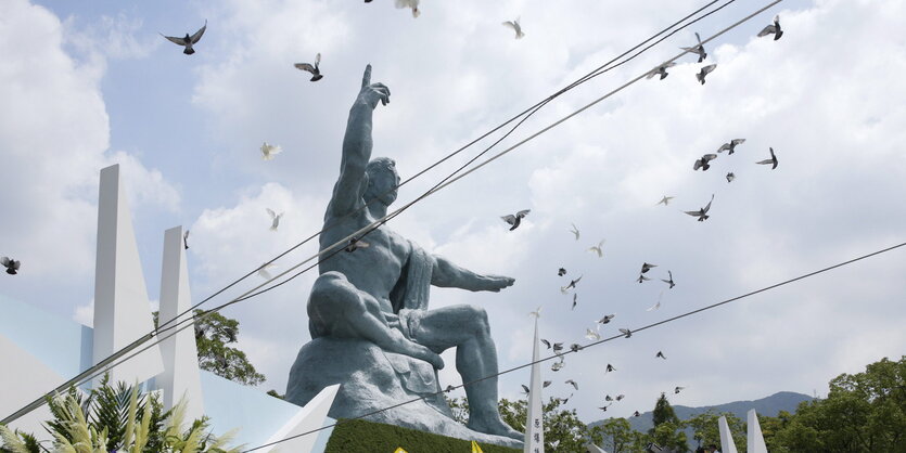 Denkmal eines auf den Himmel zeigenden Menschen, Tauben flattern drum herum