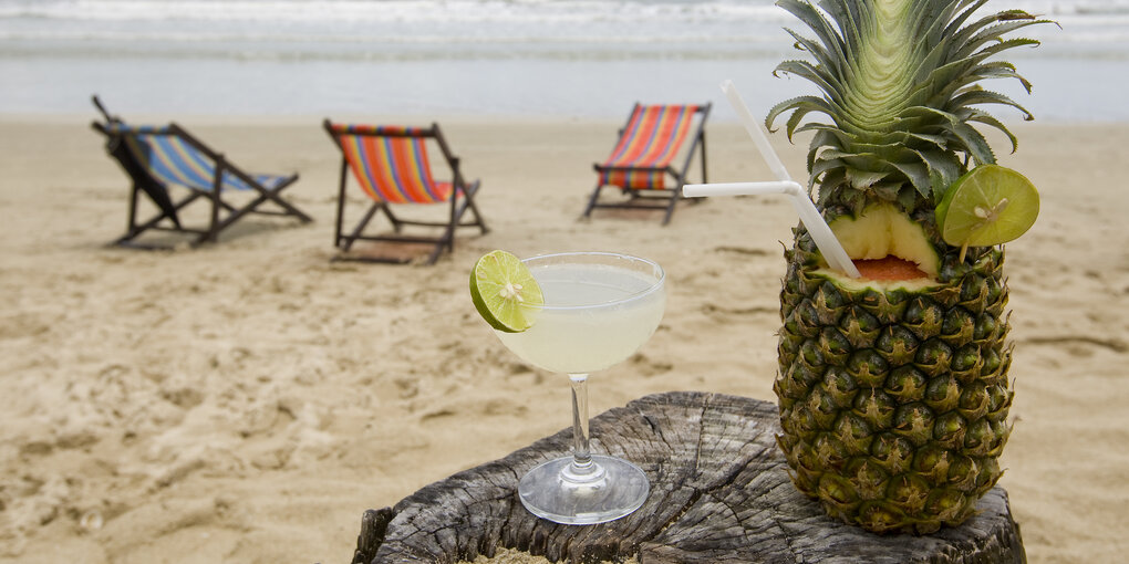 Ananas mit Strohlhalm, Cocktailglas und Liegen an einem Strand