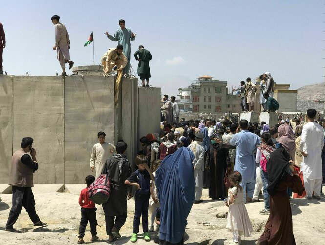 Einige Männer stehen auf einer Mauer, Kinder, Fraune und Männer davor. Flughafen Kabul