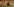 Ein Mann mit Schutzhelm und -bekleidung rennt durch ein Weizenfeld. Im Hintergrund: Flammen
