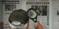 Ein Mann steht mit einer Lupe vor einer chinesischen Wandzeitung mit einem Bild von Nancy Pelosi
