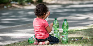 Ein Kind mit zwei Wasserflaschen sitzt auf dem Rasen