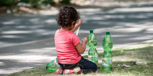 Ein Kind mit zwei Wasserflaschen sitzt auf dem Rasen