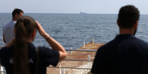 Personen schauen auf ein Frachtschiff am Horizont