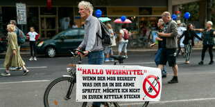 Ein Mann fährt ein Drohplakat gegen Impfärzte bei einer Demonstration mit dem Fahrrad herum