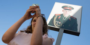 Frau macht Selfie mit Smartphone vor dem Bild eines Soldaten.