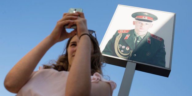 Frau macht Selfie mit Smartphone vor dem Bild eines Soldaten.