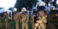 Polizisten in Kampfuniform stehen vor Zelten auf einer Wiese